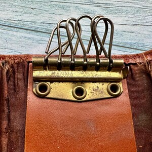 May include: A brown leather key holder with a brass key ring and the word "HANNA" engraved on the front.