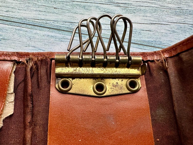 May include: A brown leather key holder with a brass key ring and the word "HANNA" engraved on the front.