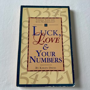 May include: A book titled "Luck, Love & Your Numbers" by Karen David. The cover features a yellow background with numbers 1 through 9 scattered across the surface. The title is written in a large, bold font with a decorative flourish on the "L" in "Love".