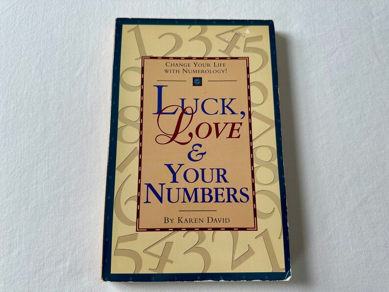 May include: A book titled "Luck, Love & Your Numbers" by Karen David. The cover features a yellow background with numbers 1 through 9 scattered across the surface. The title is written in a large, bold font with a decorative flourish on the "L" in "Love".