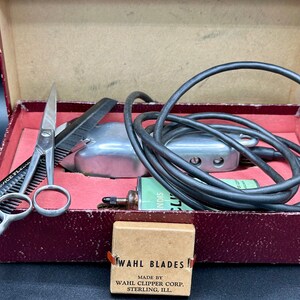 May include: A vintage red box with a silver electric hair clipper, a pair of scissors, a small can of oil, and a brown box labeled "WAHL BLADES MADE BY WAHL CLIPPER CORP. STERLING, ILL."