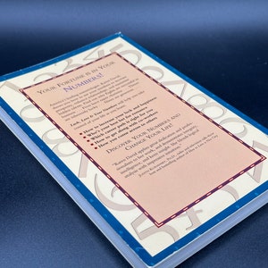 May include: A book cover with a pink and white background. The title of the book is "Your Fortune is in Your Numbers!" The book cover features a variety of numbers in a circular pattern. The book cover also includes a description of the book, which includes information about how to increase your luck and happiness, how to find your best career path, and how to get along with colleagues.