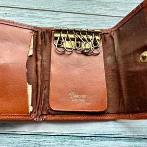 May include: A brown leather key holder with a metal key ring and the text "Baronet Cowhide" on the front.