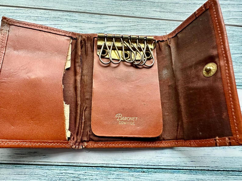 May include: A brown leather key holder with a metal key ring and the text "Baronet Cowhide" on the front.
