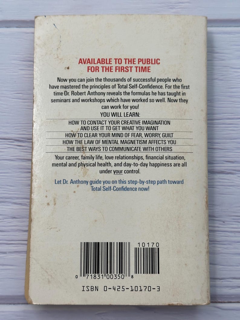 May include: A well-worn paperback book titled "Total Self-Confidence" is displayed. The cover includes the text "Available to the Public for the First Time" and a list of topics. The ISBN is 0-425-10170-3. The book shows signs of age.