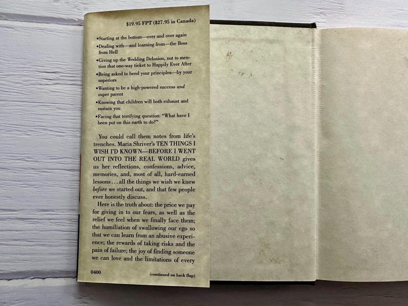 May include: An open book with text on the left page and a blank right page. The text includes the title "TEN THINGS I WISH I'D KNOWN" and a list of topics. The book is on a light-colored wooden surface.