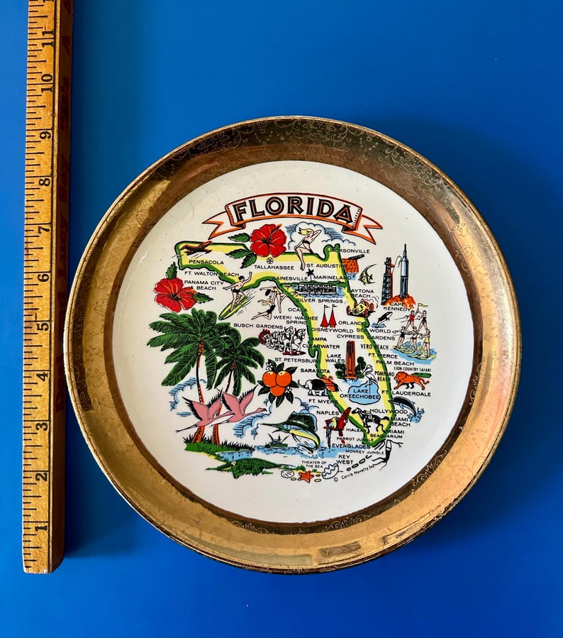 Pode incluir: Um prato de lembran&ccedil;a vintage com um mapa da Fl&oacute;rida e borda dourada. O prato exibe uma ilustra&ccedil;&atilde;o colorida do estado, incluindo cidades, pontos tur&iacute;sticos e flora. O prato tem aproximadamente 15 cm de di&acirc;metro.