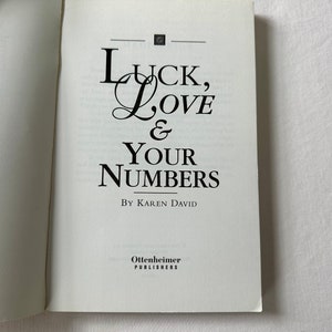 May include: A white book with the title "Luck, Love & Your Numbers" by Karen David. The book is published by Ottenheimer Publishers.