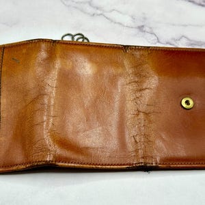 May include: A brown leather wallet with a fold-over closure and a brass button. The wallet has a worn, vintage look.