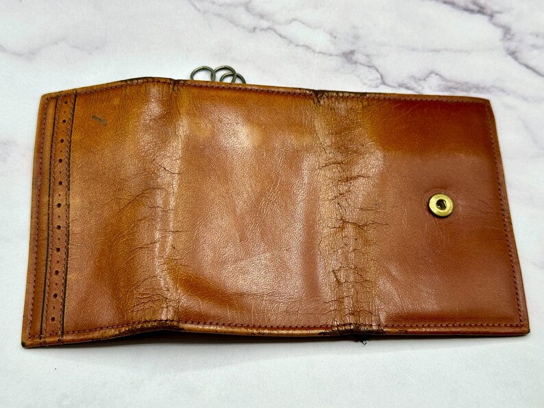 May include: A brown leather wallet with a fold-over closure and a brass button. The wallet has a worn, vintage look.