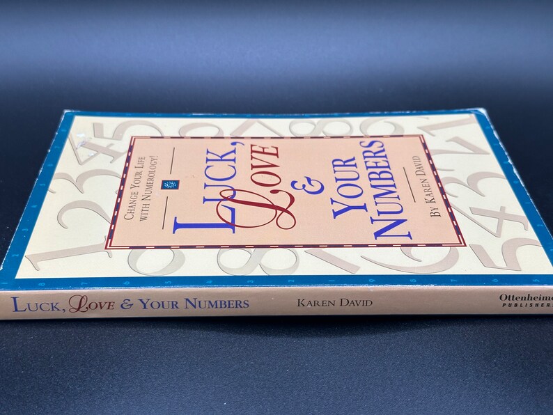 May include: A book titled "Luck, Love & Your Numbers" by Karen David. The cover features a pink and white background with a large number "1" in the background. The book is about numerology and how to change your life.