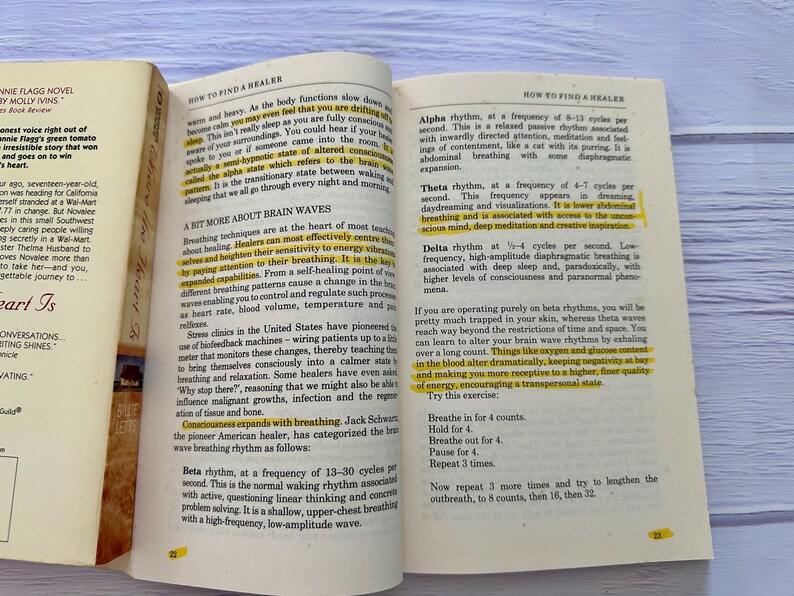 May include: Open book with text about brain waves and healing techniques. The pages are yellowed, with highlighted sections in yellow. The book is open on a light blue and white surface.