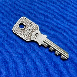 May include: A silver-colored key with the text "SKYMAKER" and the number "2710" printed on it. The key is set against a blue background.