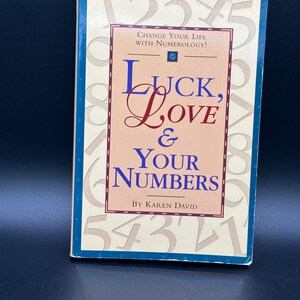 May include: A book titled "Luck, Love & Your Numbers" by Karen David. The cover features a pink background with the title in a stylised font. The cover is surrounded by numbers in a blue border.