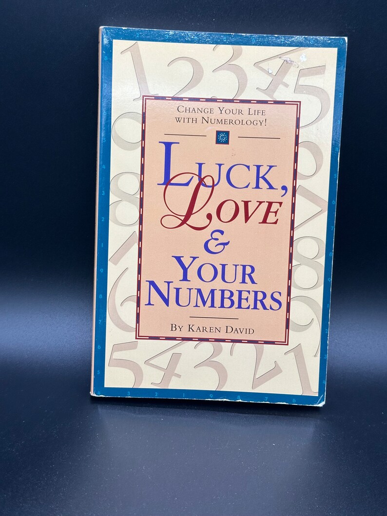 May include: A book titled "Luck, Love & Your Numbers" by Karen David. The cover features a pink background with the title in a stylised font. The cover is surrounded by numbers in a blue border.