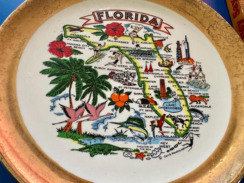 Pode incluir: Prato decorativo vintage com um mapa da Fl&oacute;rida com ilustra&ccedil;&otilde;es de marcos, flora e fauna. O prato tem um centro branco com uma borda dourada e o texto "Florida" no topo.