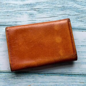May include: A brown leather wallet with a worn, distressed look. The wallet is closed and has a stitched edge.