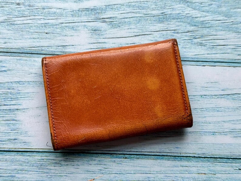 May include: A brown leather wallet with a worn, distressed look. The wallet is closed and has a stitched edge.