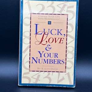 May include: A book titled "Luck, Love & Your Numbers" by Karen David. The cover features a background of numbers and the title in a red, white, and blue colour scheme. The book is about using numerology to change your life.