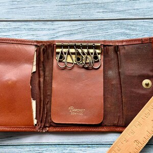 May include: A brown leather key holder with a metal key ring and the text "Baronet Cowhide" on the front.