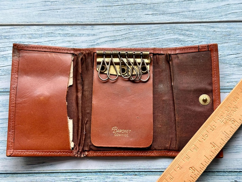 May include: A brown leather key holder with a metal key ring and the text "Baronet Cowhide" on the front.