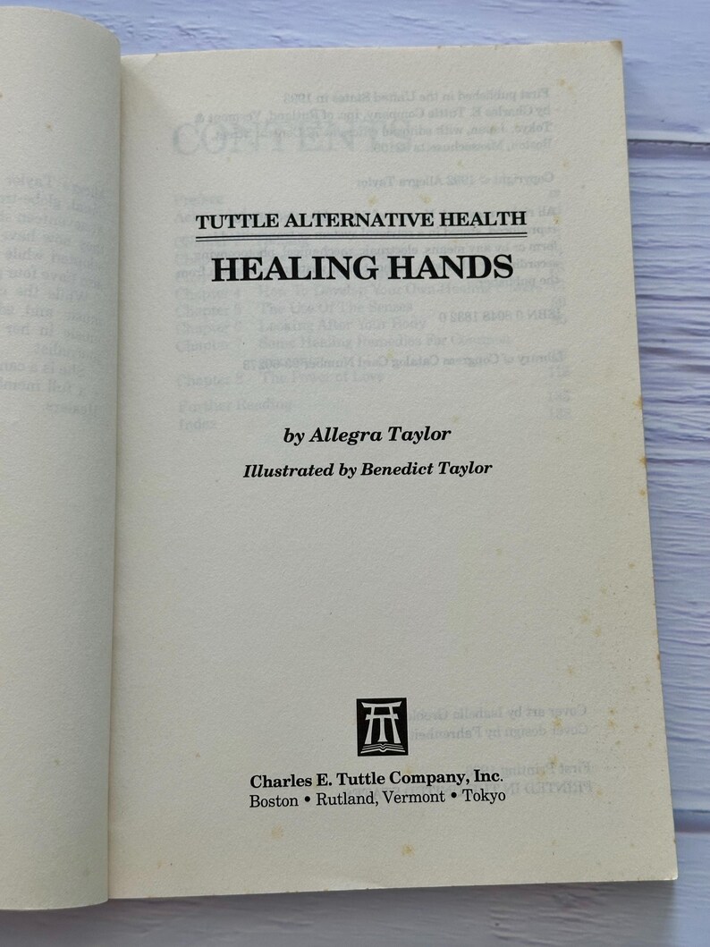 May include: Open book with the title "Healing Hands" by Allegra Taylor. The book is published by Charles E. Tuttle Company, Inc. The cover is off-white with black text. The book is open to the title page.