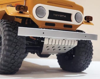 May include: A close-up of a yellow toy truck with a silver front bumper and a black skid plate. The truck has a white grill with the word "TOYOTA" printed on it.