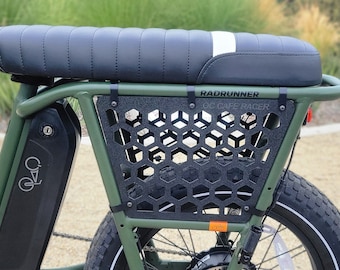 Puede incluir: Una bicicleta eléctrica verde con un asiento de cuero negro y un portaequipajes de metal negro con un patrón de panal. La bicicleta tiene una batería negra con un logotipo que dice "Radrunner OC Cafe Racer".