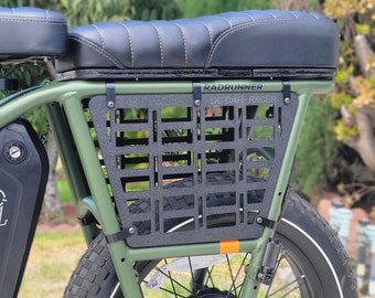 Puede incluir: Una bicicleta eléctrica verde con un asiento de cuero negro y un portaequipajes de metal negro con una inserción de malla. La bicicleta tiene una pegatina en blanco y negro que dice "Radrunner OC Cafe Racer".
