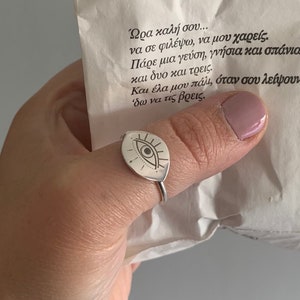 May include: Silver ring featuring an eye design. The ring is worn on a finger and the eye is detailed with lines and a pupil.