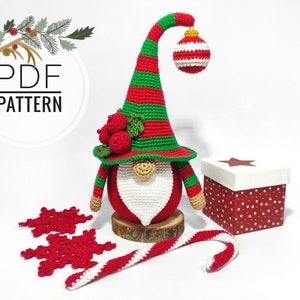 May include: A handmade crochet Christmas gnome with a red and green striped hat, a white beard, and a red body. The gnome is decorated with red berries and a hanging ornament. Includes a candy cane, snowflakes, and a gift box.