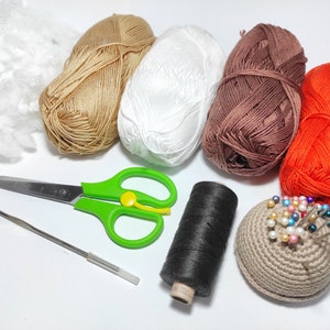 May include: A collection of yarn in various colors, including brown, white, orange, and black, along with a crochet hook, scissors, and a pincushion.