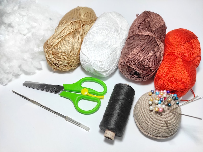 May include: A collection of yarn in various colors, including brown, white, orange, and black, along with a crochet hook, scissors, and a pincushion.