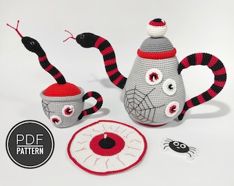 May include: A crocheted tea set featuring a teapot, cup, saucer, and spider. The teapot and cup are decorated with red and black stripes and have a spiderweb design with white eyes. The saucer is a red and white eye design. The spider is white with black eyes.