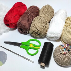 May include: A collection of yarn in various colors, including red, brown, beige, and white, along with a crochet hook, scissors, a spool of black thread, a crocheted pincushion, and a piece of stuffing.