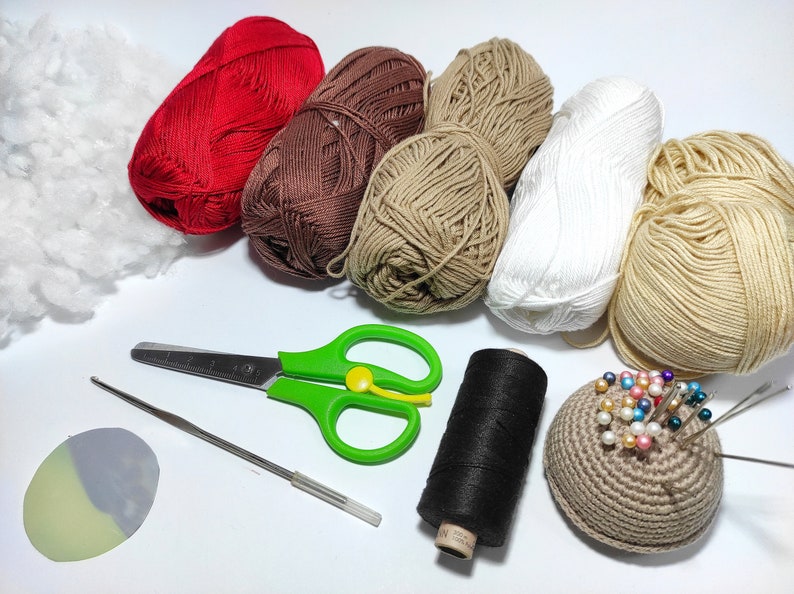 May include: A collection of yarn in various colors, including red, brown, beige, and white, along with a crochet hook, scissors, a spool of black thread, a crocheted pincushion, and a piece of stuffing.