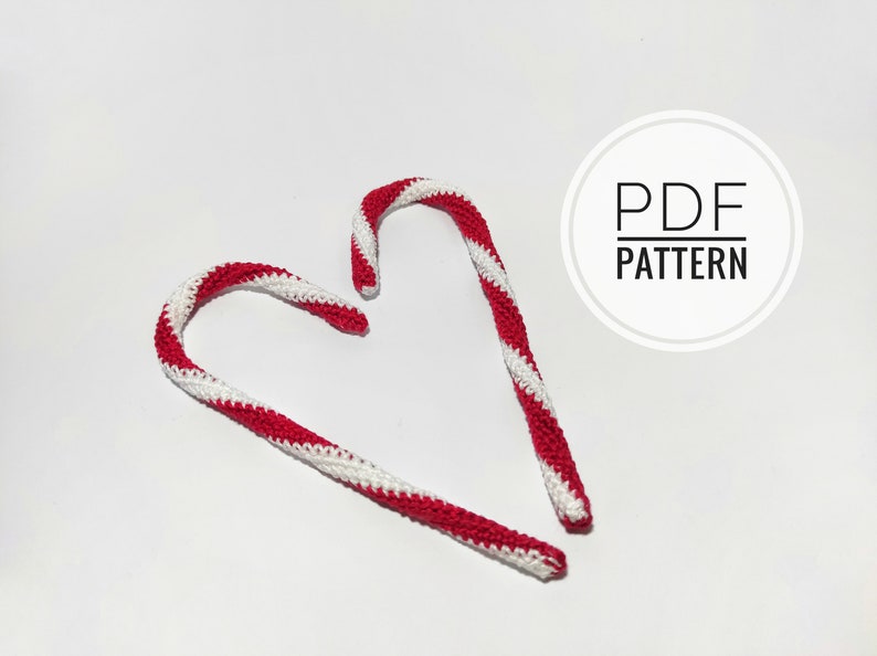 May include: Two crocheted candy canes with red and white stripes, arranged on a white background. The text "PDF PATTERN" is in a white circle in the upper right corner. These decorative candy canes are perfect for holiday crafting.