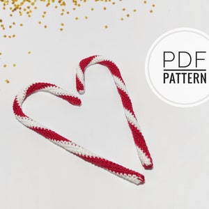 May include: Two handmade crochet candy canes with red and white stripes, arranged on a white surface. The text "PDF PATTERN" is in a white circle. Gold glitter is scattered in the background.