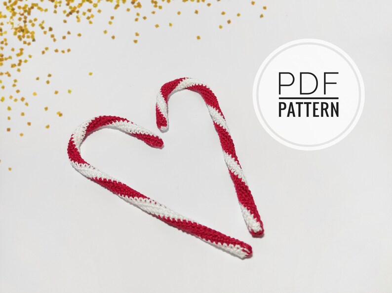 May include: Two handmade crochet candy canes with red and white stripes, arranged on a white surface. The text "PDF PATTERN" is in a white circle. Gold glitter is scattered in the background.