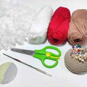 May include: A collection of crafting supplies including white, red, and brown yarn, a pincushion, scissors, a crochet hook, and stuffing.