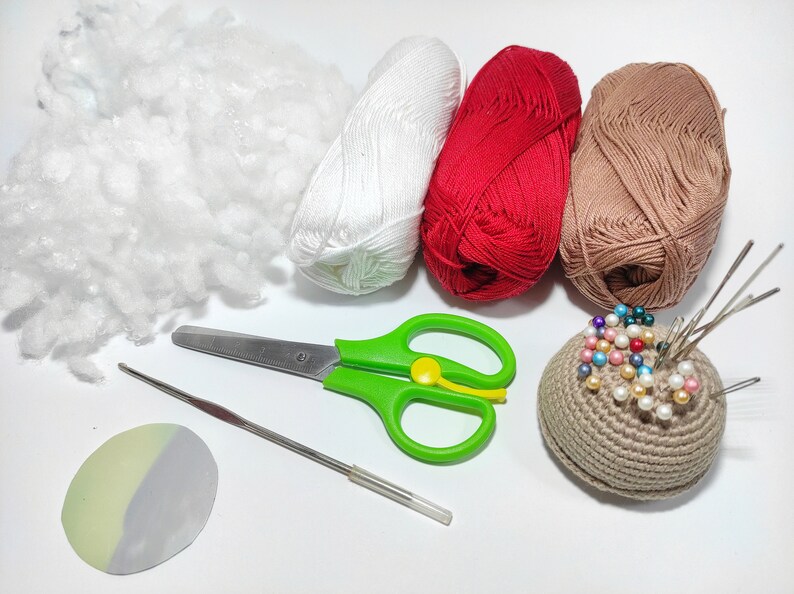 May include: A collection of crafting supplies including white, red, and brown yarn, a pincushion, scissors, a crochet hook, and stuffing.
