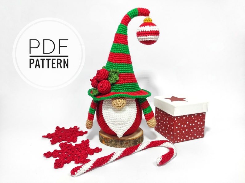 May include: A crocheted Christmas gnome with a red body, white beard, and a green and red striped hat. The hat has a hanging ornament. Includes a gift box, snowflakes, and a candy cane. The text "PDF PATTERN" is in a circle.