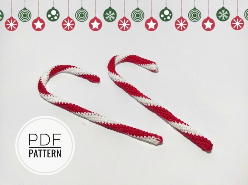 May include: Two crocheted candy canes with red and white stripes. The candy canes are curved and have a textured appearance. The image also includes a decorative border of Christmas ornaments and the text "PDF PATTERN".