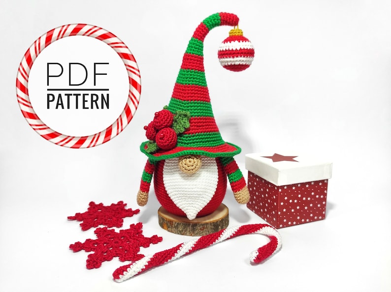 May include: A handmade crochet Christmas gnome with a red and green striped hat, a white beard, and a red body. The gnome is decorated with a red ornament and berries. Includes a candy cane, snowflakes, and a gift box. The image also includes the text "PDF PATTERN".