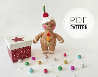 May include: Crochet gingerbread man amigurumi toy with a red cherry on top, white icing, and colorful buttons. The toy is surrounded by small colorful balls and a red and white gift box with a star on top. The text "PDF PATTERN" is visible in a white circle.