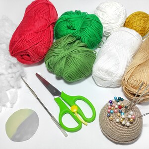 May include: A collection of craft supplies for crocheting or knitting, including red, green, white, and tan yarn balls, stuffing, a crochet hook, scissors, a pin cushion with pins, and a small, two-tone disc.