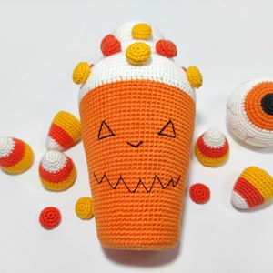 May include: A crocheted orange and white Halloween-themed candy corn with a jack-o'-lantern face, surrounded by smaller crocheted candy corn and a crocheted eyeball.