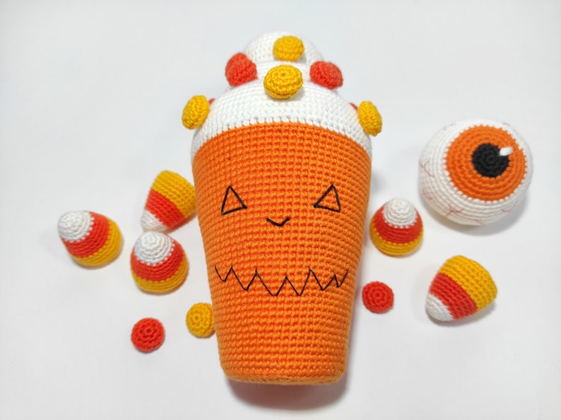 May include: A crocheted orange and white Halloween-themed candy corn with a jack-o'-lantern face, surrounded by smaller crocheted candy corn and a crocheted eyeball.