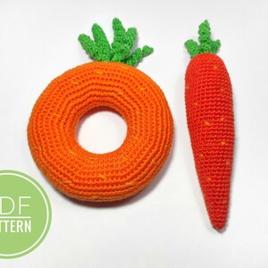 Puede incluir: Dos zanahorias de crochet, una es un anillo y la otra es una zanahoria larga. Ambas son de color naranja con tapas verdes. El texto "PDF PATTERN" est&aacute; en un c&iacute;rculo verde.