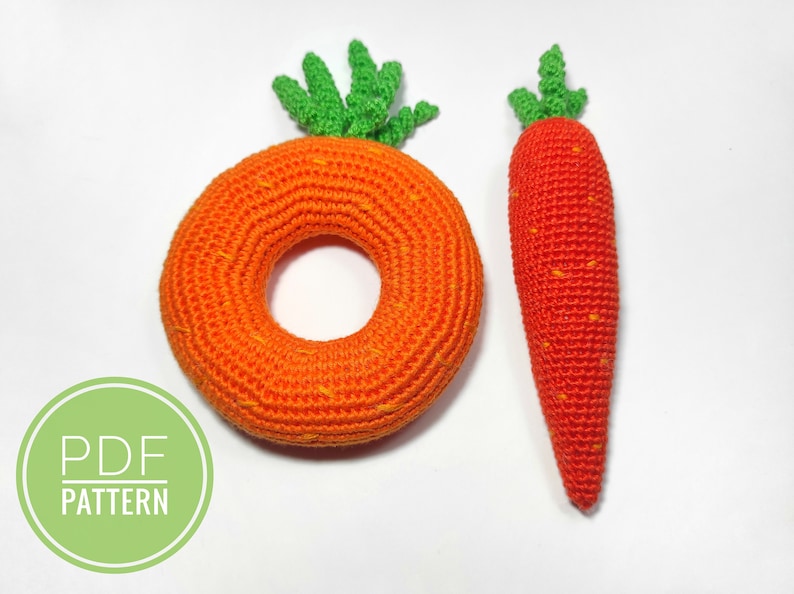 Puede incluir: Dos zanahorias de crochet, una es un anillo y la otra es una zanahoria larga. Ambas son de color naranja con tapas verdes. El texto "PDF PATTERN" est&aacute; en un c&iacute;rculo verde.